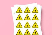A stack of white sheets featuring yellow triangular warning labels with black lightning bolt symbols, set against a solid pink background.