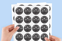 A pair of hands holding a stack of white sticker sheets printed with repeated black circular logos reading 'MEL & CLOUD LOW & SLOW' against a light blue background.

